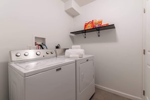 A laundry area with a front-loading washer and dryer, a shelf with laundry detergent, and a towel rack. - The Greenhouse: Modern Rural Escape with Fire Pit (Ithaca)