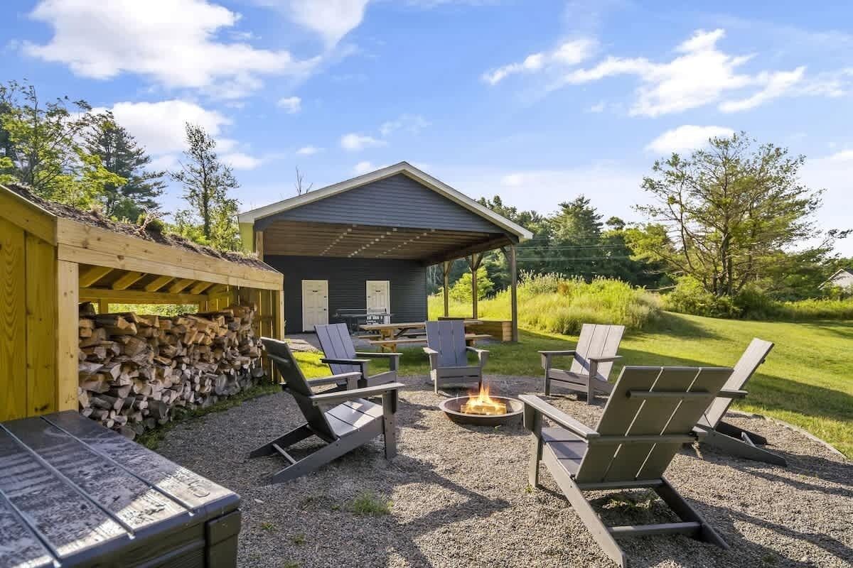 Ein Sitzbereich im Freien mit Adirondack-Stühlen und einer Feuerstelle, umgeben von einer Holzterrasse und einer überdachten Struktur.