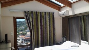 A bedroom with a bed, a TV, a balcony with a view of the town, and a skylight. - Aria Hotel (Skiathos)