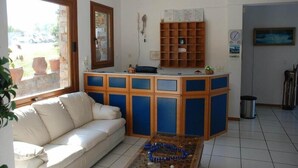 A living room with a sofa, a coffee table, a wooden cabinet, and a window. - Aria Hotel (Skiathos)