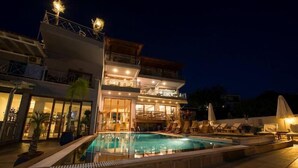 A multi-story hotel with a swimming pool, outdoor seating, and a well-lit facade. - Aria Hotel (Skiathos)