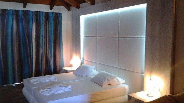 A hotel room with a large bed, a wooden ceiling, and a nightstand with a lamp. - Aria Hotel (Skiathos)