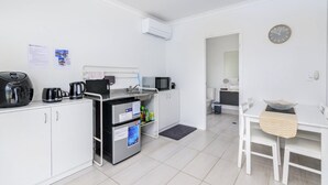 Una kitchenette compacta con cafetera, microondas y refrigerador. Hay un pequeño comedor con una mesa y sillas.