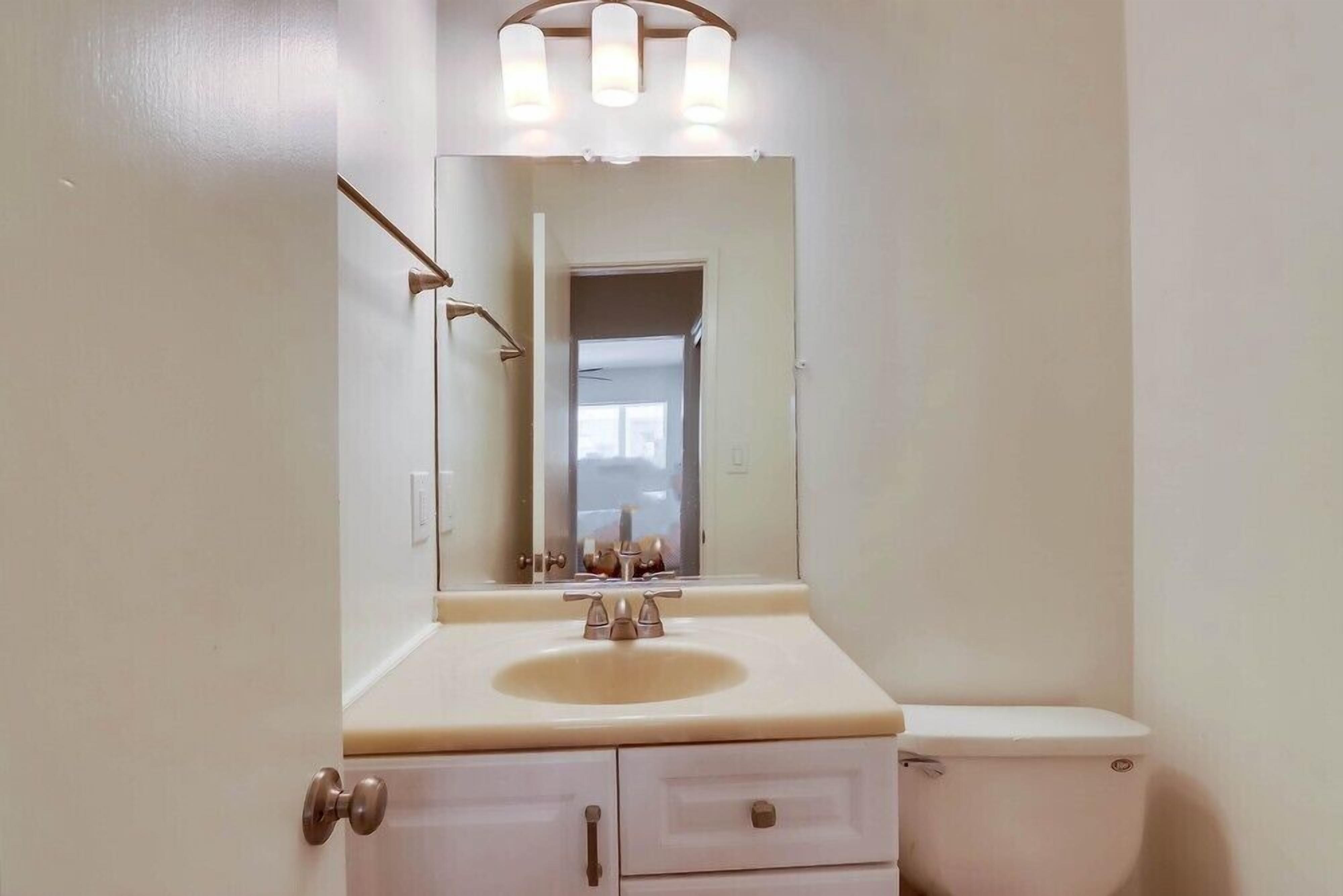 A bathroom with a white sink, mirror, and toilet.