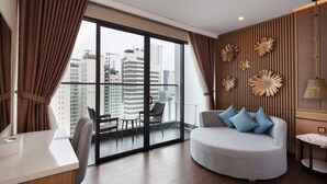 A modern hotel room with a large balcony, a round grey sofa with blue cushions, a wooden floor, and a city view. - Virgo Hotel (Nha Trang)