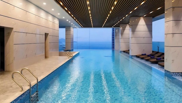 A modern indoor swimming pool with a clear view of the sky, surrounded by marble walls and a ceiling with linear lighting. - Virgo Hotel (Nha Trang)