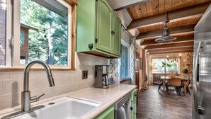 A modern kitchen with a large sink, green cabinets, and a dining area with a wooden table and chairs. - Mv30 unique Lake Tahoe cabin with great wifi (South Lake Tahoe)