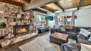 A cozy living room with a stone fireplace, wooden beams, and a large window offering a view of the outdoors. - Mv30 unique Lake Tahoe cabin with great wifi (South Lake Tahoe)