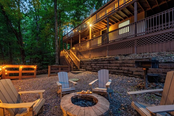 A cabin with a fire pit, Adirondack chairs, and a staircase leading to a balcony.