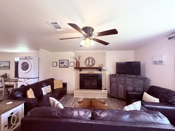 A living room with a fireplace, leather sofas, a television, and a ceiling fan.