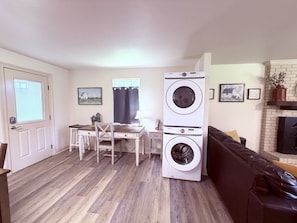 A compact living space with a dining area, a sofa, a fireplace, and a stacked washer and dryer. - Farm House stay with soaking tub and hot tub barn (Tickfaw)