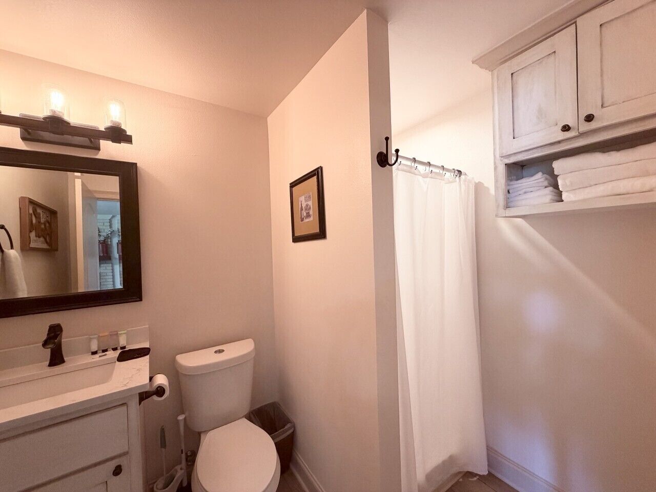 A bathroom with a toilet, sink, mirror, and a cabinet with towels.