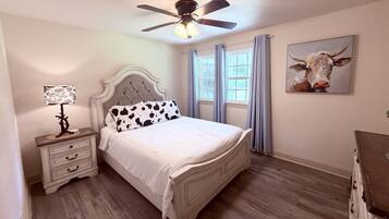 A bedroom with a bed, a nightstand, a ceiling fan, and a window with curtains.