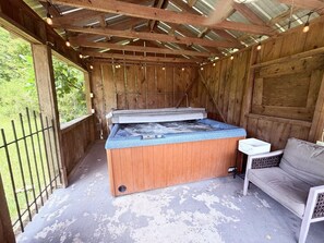 A hot tub with a wooden exterior and a metal frame, situated in a covered outdoor area with a wooden bench and a small table. - Farm House stay with soaking tub and hot tub barn (Tickfaw)