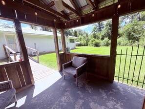 A covered outdoor area with a wooden deck, a single chair, and a view of a house and lawn.