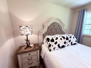 A bedroom with a bed, a nightstand with a lamp, and a window with curtains.