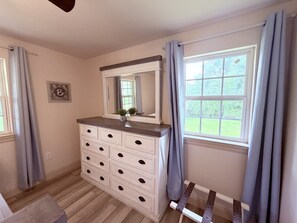 Een slaapkamer met een dressoir, een raam met gordijnen en een spiegel.