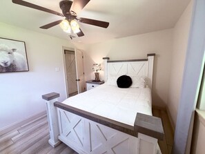 A bedroom with a bed, a ceiling fan, a nightstand, and a door. - Farm House stay with soaking tub and hot tub barn (Tickfaw)
