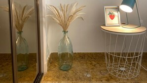 Een badkamer met een marmeren aanrecht, een spiegel, twee glazen vazen met gedroogd pampa gras, een ingelijst beeld met een hart en het woord 'LOVE', en een klein tafeltje met een blauwe lamp.