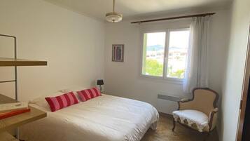 A bedroom with a bed, a chair, a desk, and a window.