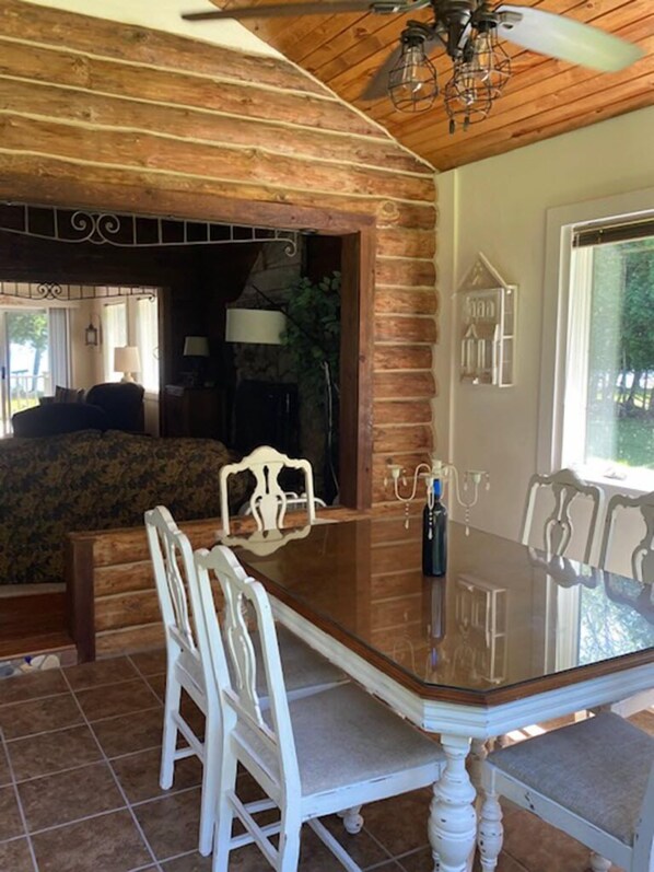 A dining area with a wooden table and white chairs, a chandelier, and a view of the outdoors.
