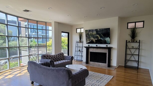 A modern living room with a fireplace, large windows, and a flat-screen TV.