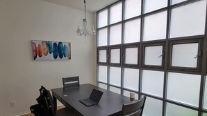 A dining area with a table, chairs, a laptop, a coffee cup, a chandelier, and a large window with frosted glass panels.