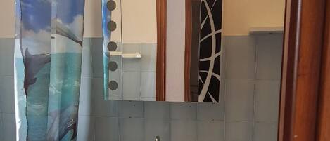 Ein Badezimmer mit einem weißen Waschbecken, einem Spiegel mit geometrischer Rahmen und einem Duschvorhang mit Delphin-Motiv.