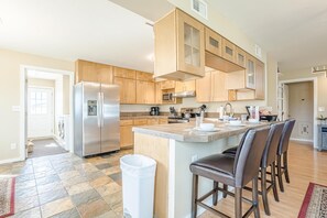 Eine moderne Küche mit Holzschränken, einem Edelstahlkühlschrank, einer Mikrowelle und einer großen Kochinsel mit Barhocker.