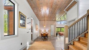 Un hall d’entrée spacieux avec un escalier en bois, un tapis et un coin repas comprenant une table et des chaises.