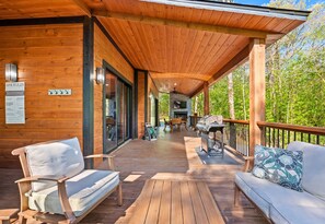 A wooden deck with a covered area, outdoor seating, and a grill.