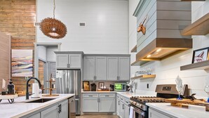 Une cuisine moderne avec des meubles gris, des appareils en acier inoxydable et un luminaire suspendu.