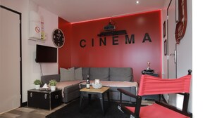 A living room with a red wall, a sofa, a small table, a television, and a projector. - Cinema apartment with home cinema and garage (Honfleur)