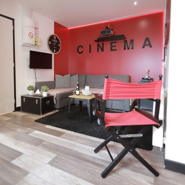Ein modernes Wohnzimmer mit einer roten Akzentwand, einem Sofa, einem Couchtisch, einem Fernseher und einem Projektor.