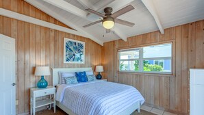 Ein Schlafzimmer mit einem Bett, zwei Nachttischen, einem Deckenventilator, einem Fenster und einer Tür.