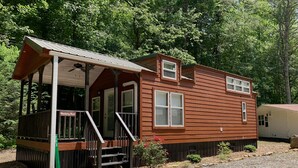 A wooden cabin with a porch, a covered deck, and a small garden area. - Tiny Home only 1 mile to Vogel State Park!  Wandering Wood at the Reece Farm Vlg (Blairsville)