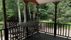 A covered outdoor area with a wooden deck, metal chairs, and a round table. - Tiny Home only 1 mile to Vogel State Park!  Wandering Wood at the Reece Farm Vlg (Blairsville)