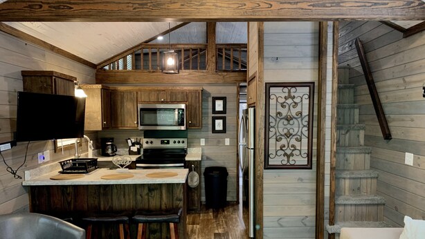 A rustic kitchen with wooden beams, a built-in microwave, and a bar area with stools. - Tiny Home only 1 mile to Vogel State Park!  Wandering Wood at the Reece Farm Vlg (Blairsville)