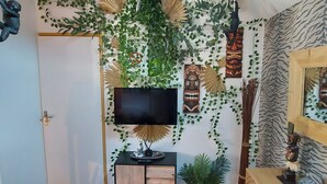 Ein Zimmer mit an der Wand befestigtem Fernseher, umgeben von dekorativen Stammesmasken und Grünpflanzen.