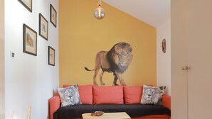 Ein Wohnzimmer mit einem roten Sofa, einer Löwen-Mural, gerahmten Bildern, einer Hängelampe und einem weißen Teppich.