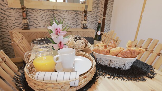 Ein Frühstücksangebot mit einem Korbtablett, das Croissants, eine Champagnerflasche, Orangensaft in einem Glas und eine weiße Tasse enthält.