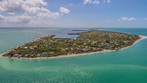 An aerial view of a coastal island with dense vegetation, numerous houses, and clear turquoise waters.