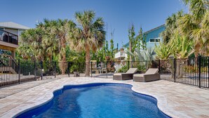 A swimming pool with a curved edge, surrounded by a black metal fence, and palm trees.