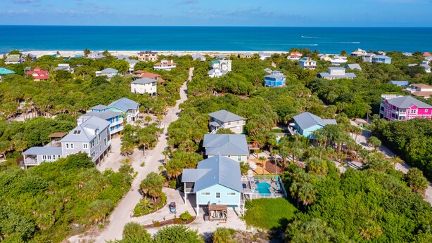 An aerial view of a coastal residential area with houses, a beach, and a clear blue sky.