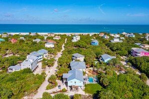 An aerial view of a coastal residential area with houses, a beach, and a clear blue sky.