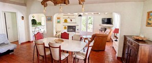 A dining area with a round table and chairs, a sofa, a television, and a fireplace.