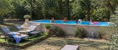 An outdoor swimming pool area with lounge chairs and a table, surrounded by trees.