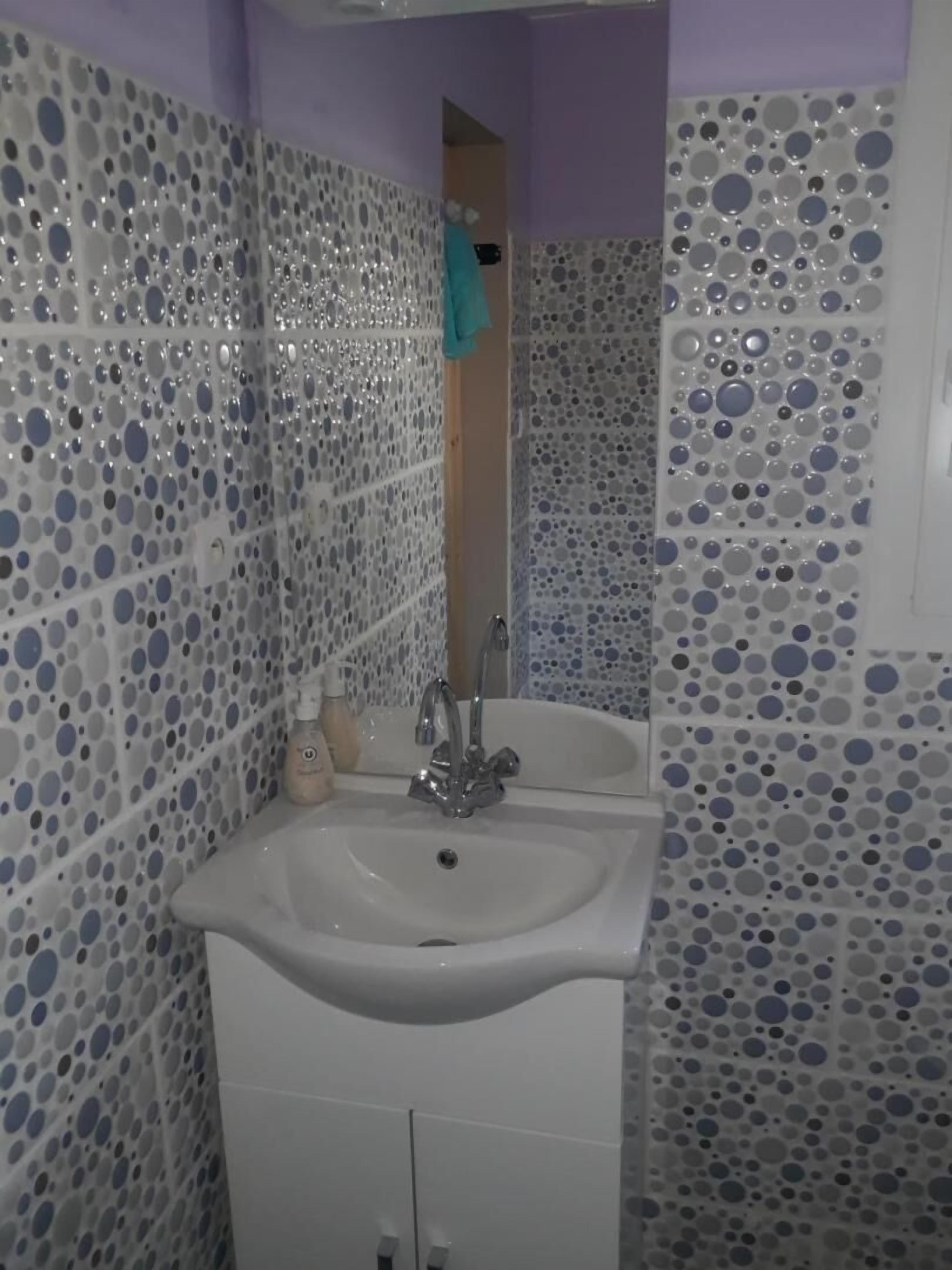 Ein Badezimmer mit weißem Waschbecken, Spiegel und Fliesenwänden mit einem Rundmuster.