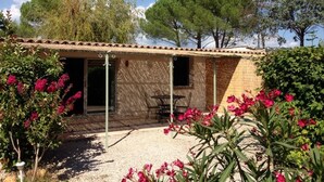 A small building with a tiled roof, a patio area with a table and chairs, and a garden with flowering plants.
