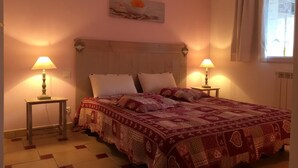 A bedroom with a wooden headboard, two bedside lamps, a patterned bedspread, and a painting above the bed.